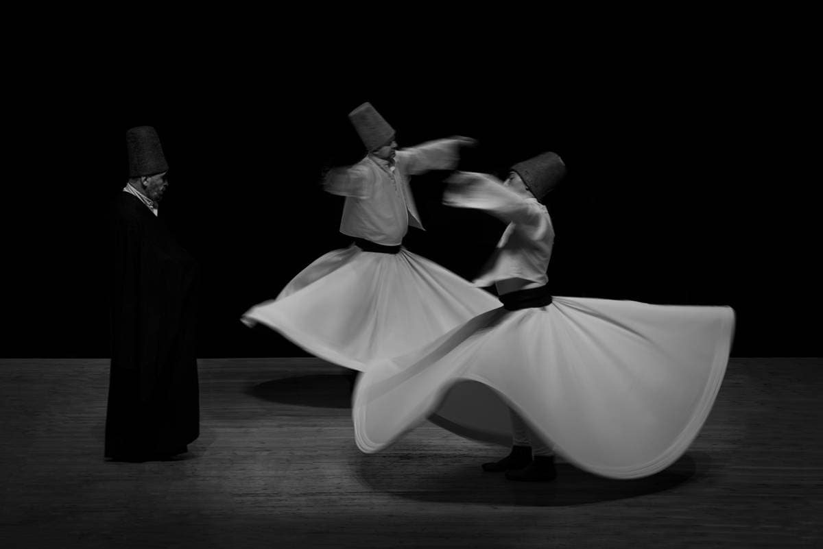 Three figures during a whirling performance against a dark background