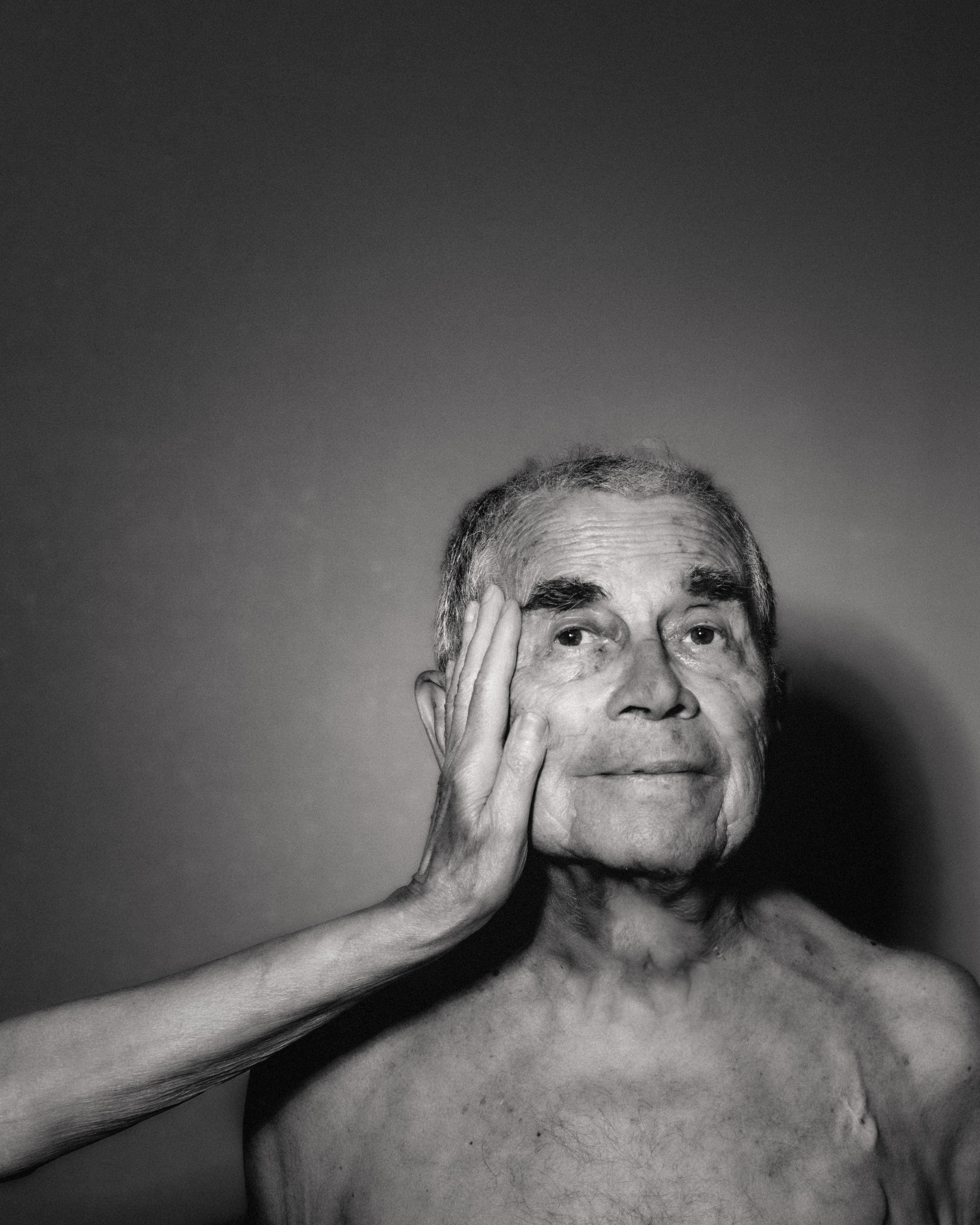 A man with his hand resting against his face in a black-and-white portrait