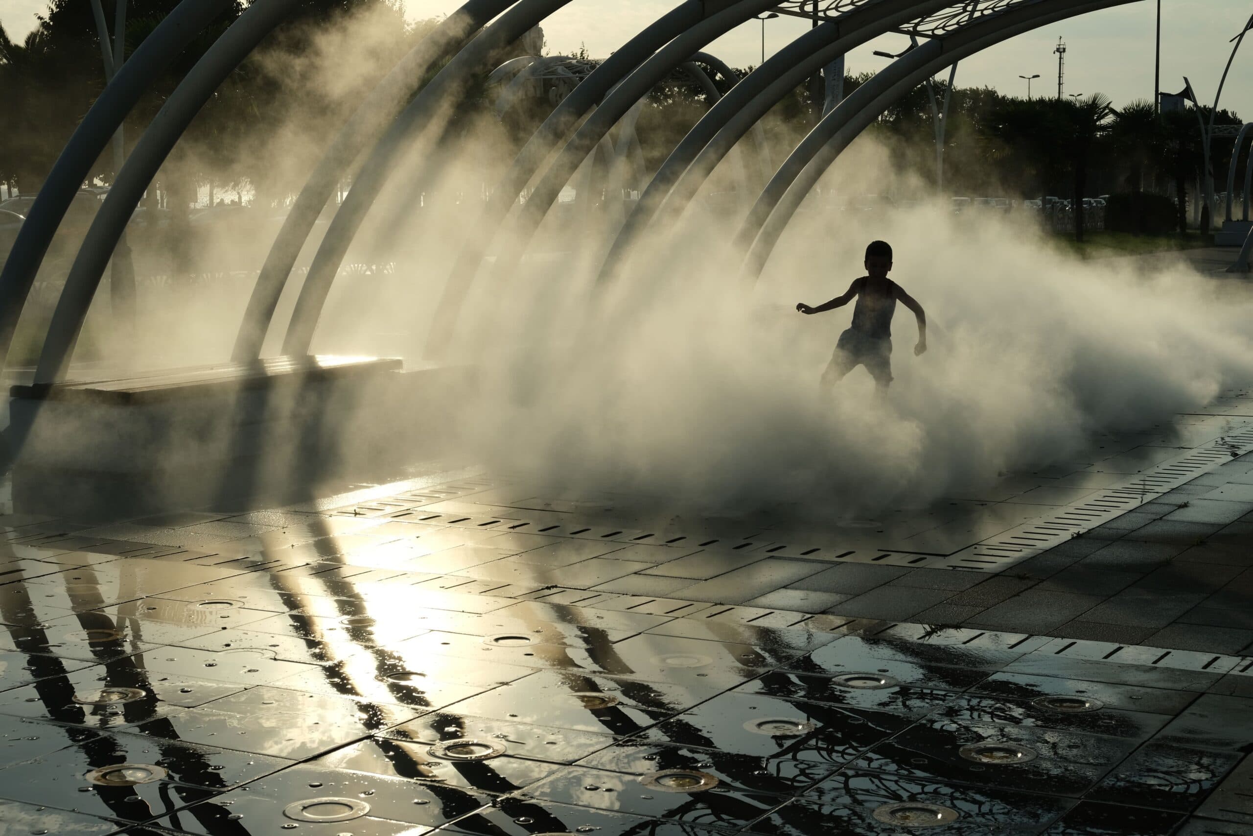 A child moving through sunlit mist beneath a row of curved structures