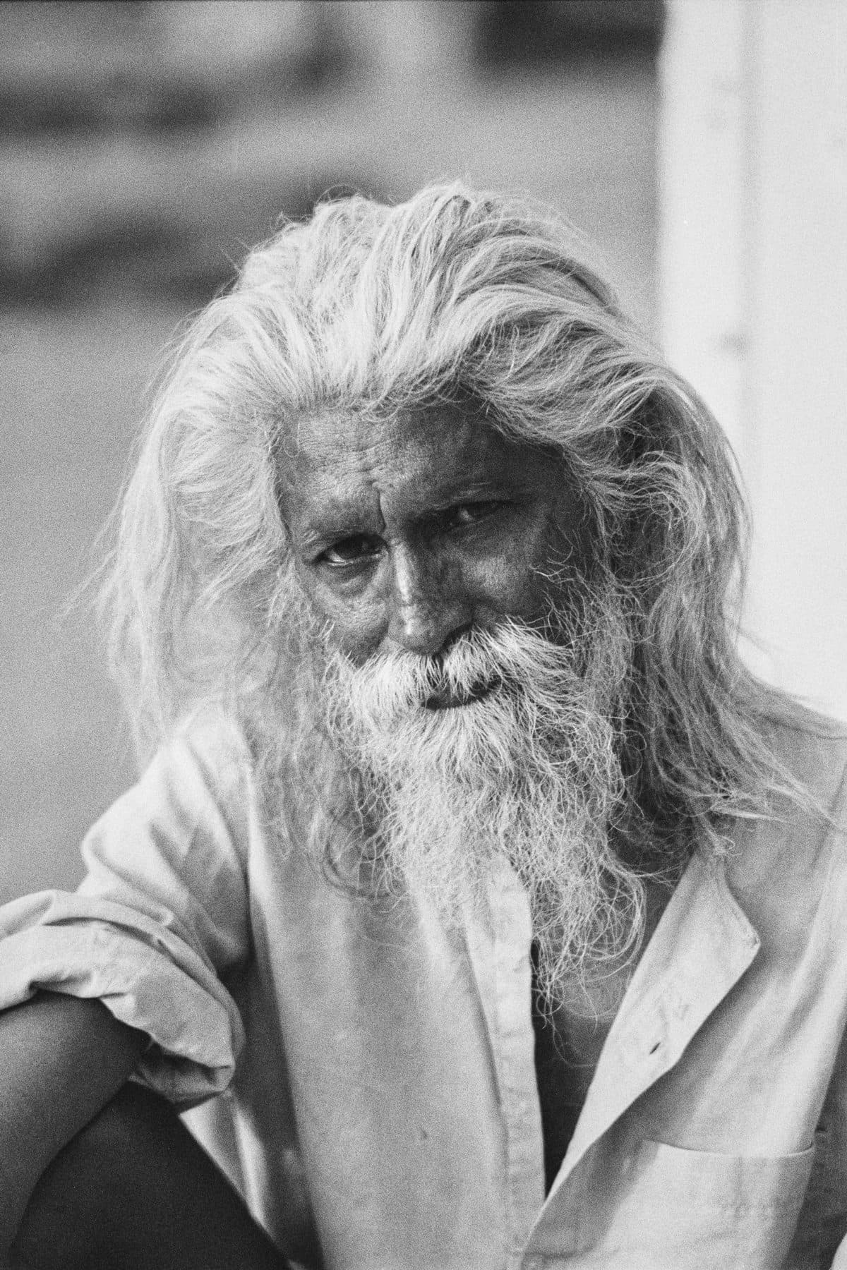 A close black-and-white portrait of a man with long white hair and a beard