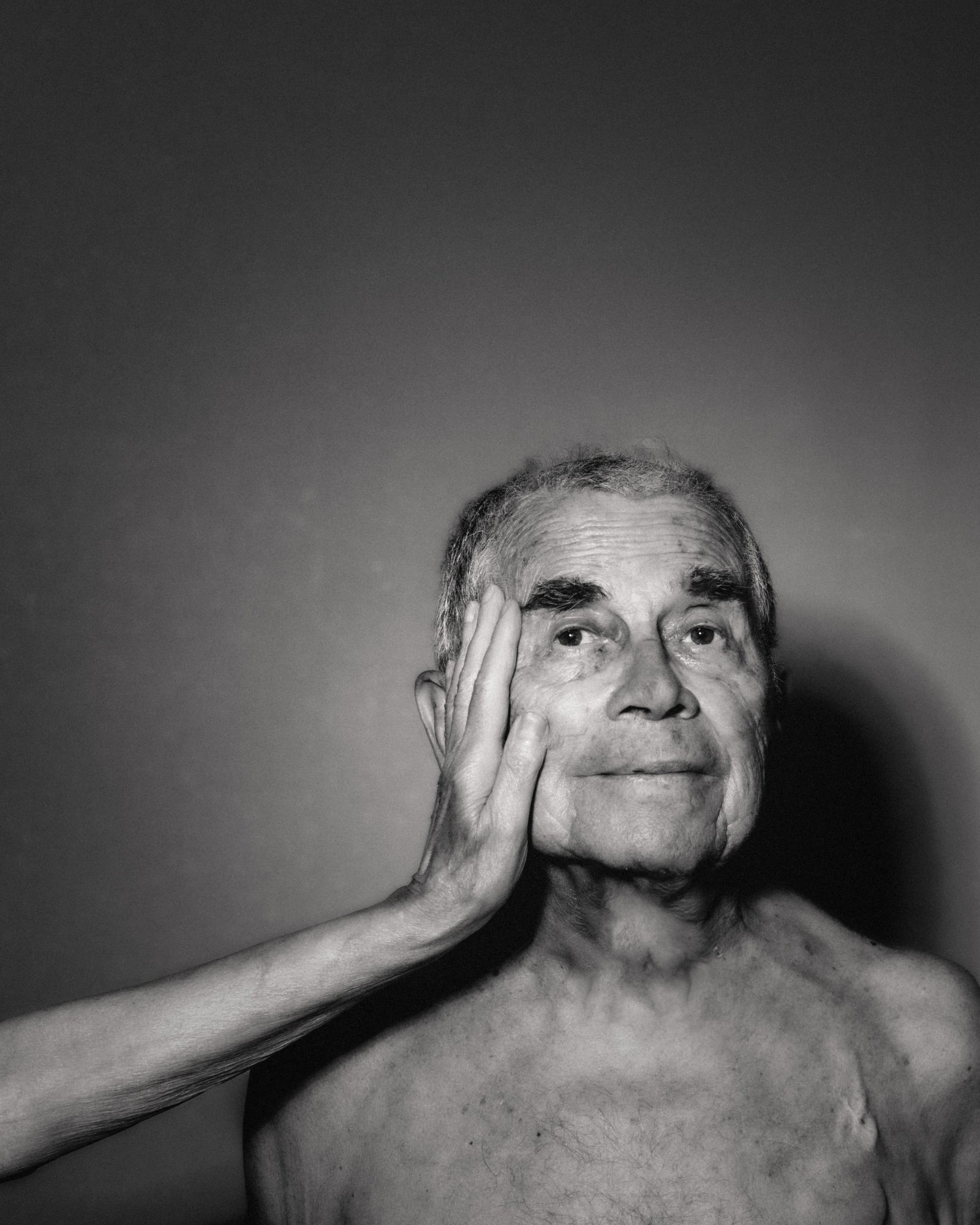 A man with his hand resting against his face in a black-and-white portrait