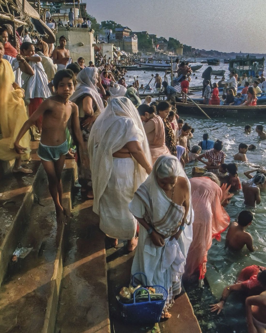 Layered documentary photograph of people gathered along the river and bathing in Varanasi