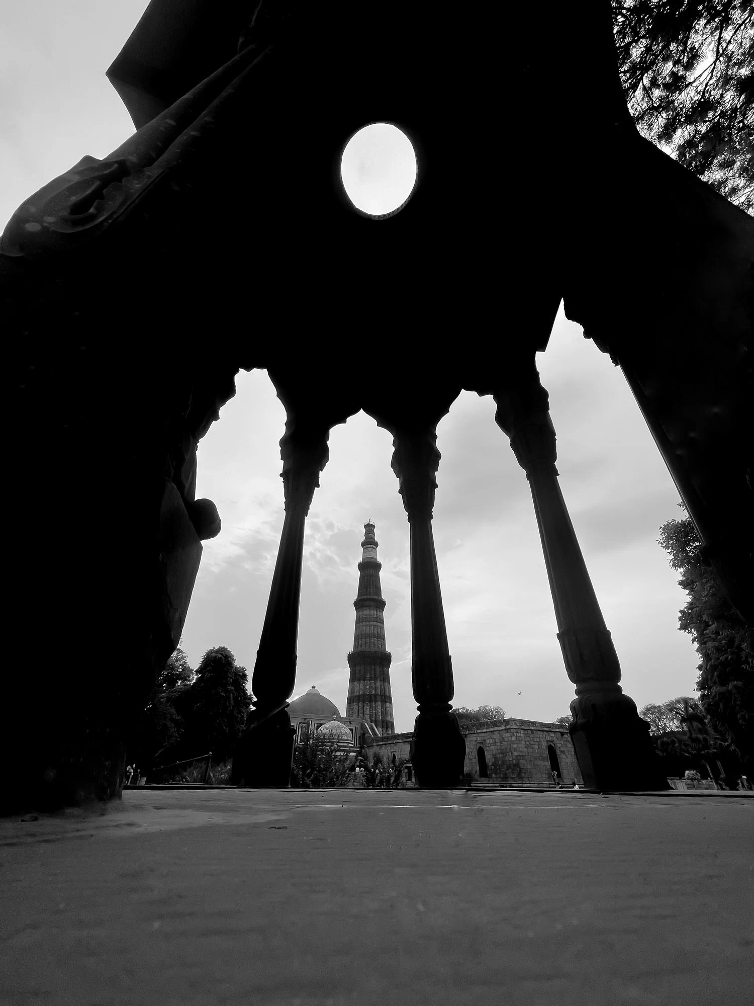 Qutub Minar framed through the arches of a dark pavilion, photographed by Priya Ojha