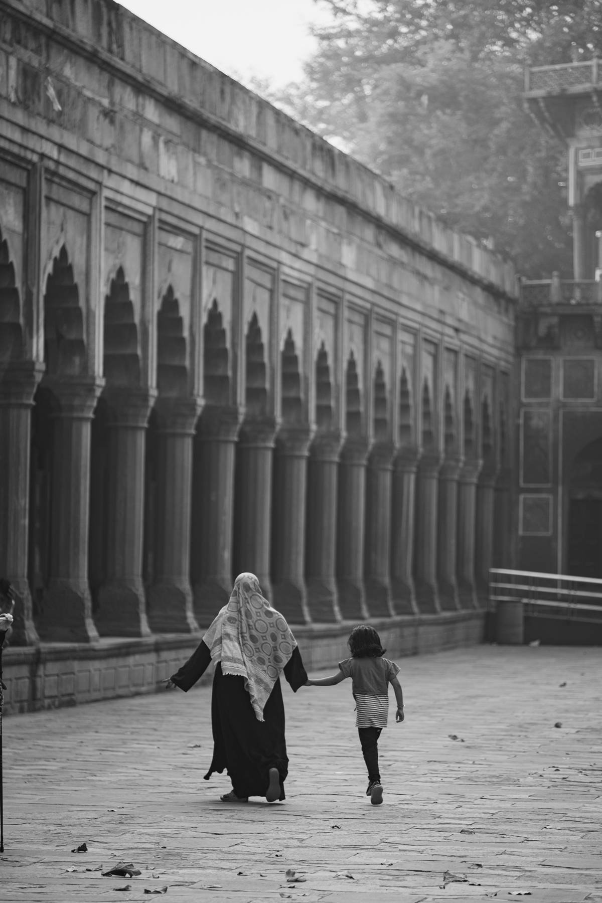 A woman and child walking together beneath a long arcade